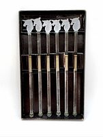 Top-down view of the full set of six frosted unicorn head glass swizzle sticks arranged in original black packaging.