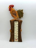 Front view of the handcarved wooden rooster thermometer showing the rooster painted in vibrant colors and the embedded temperature scale in Celsius and Fahrenheit.