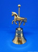 Front side view of the vintage brass carousel unicorn bell on a blue background, showing sculpted unicorn figure and bell base.