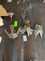 Photo of all three Art Deco metal ceiling fixtures placed on wooden floor, showing top view and overall condition. Various decorative elements and wire hangers visible.