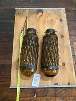 Pair of amber blown glass pendant light shades laid flat on wood, with a tape measure showing length around 17 inches.