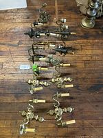 Top down photo showing multiple wall sconces laid out on a wooden floor, varying types including double-arm and single-arm sconces in bronze, brass, and cast iron.