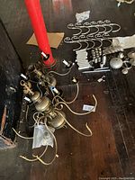 Three chandeliers disassembled and laid out on dark wood floor. Various chandelier parts including curved arms, electrical sockets, and finials visible.