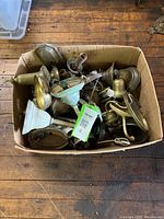 Box containing multiple brass electric wall sconce parts piled together in no particular order, showing various base plates and arms.