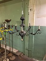 Front view of five arm wrought iron chandelier hanging from chain, showing curved arms and candle style lights.