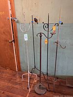 Five adjustable wrought iron bridge floor lamps together showing variety of bases and finishes in a row against a wall.