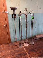 View showing all 7 antique floor lamps including torchieres and bridge lamp styles, positioned against wall on wooden floor.