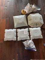 View of all five glass light fixture panels laid on wood floor: three matching small square panels, one large square panel, one large octagonal panel, and several metal fixture bases wrapped in plastic bags.