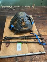 Overall view of the antique bronze hanging bowl light fixture laid on a wooden surface alongside three matching decorative rods wrapped with blue tape.