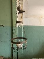 Full view of the hanging oil light suspended from ceiling, showing the decorative metal top plate, chain suspension, the ring with glass bead dangles, and the hand-painted glass reservoir bowl.