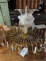 Photo showing full chandelier frame with candle-style bulb holders and curved metal arms, crystals wrapped in plastic in the center.