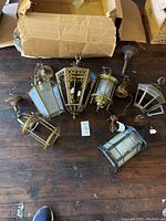 Seven brass hanging lanterns arranged on wooden floor, some missing glass panes.