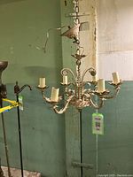 Full view of chandelier hanging against a green and white wall, showing 6 arms with candle lights and chain suspension