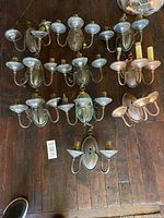 Overview of all nine 3-arm brass wall sconces arranged on wooden floor, showing aged patina and varied mounting details.