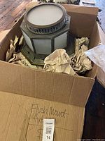 Octagonal pierced tin flush mount fixture in cardboard box with packaging paper, showing top vented portion and frosted glass diffuser.