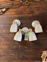 Top-down view of two single-light and one double-light white and gold mid century wall sconces with original wiring and hardware on wooden floor.