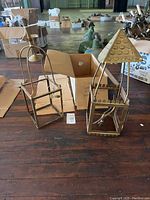 Pair of brass gas lanterns on the floor with one lantern having a shingle top and the other curved top, near cardboard boxes.