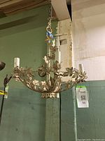 Full view of white tole metal chandelier suspended, showing the shape and decorative leaves and flowers.