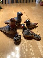 Photo showing all five ceramic bird figurines arranged on wood table, varying sizes and colors visible.
