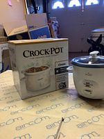 Photo showing boxed Crock-Pot Classic slow cooker and Rival rice cooker appliance side by side on a table.