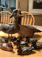 All nine ducks displayed on a table: one large metal duck, one large fabric duck, seven small wooden ducks