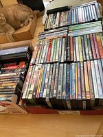 Photo showing a large collection of DVDs stacked on a table with a cat nearby, showing over 100 DVDs including boxed sets and individual movie titles.