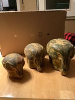 Front view of the three pottery elephants arranged by size on floor in front of cardboard background.