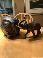 Two resin elephant figurines on a wooden table, one facing forward with trunk raised and one facing backward.