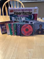 Photo showing the 26-piece Giant Ocean Creatures floor puzzle box, suitable for ages 3+, alongside 14 children's music CDs including Erick Traplin albums.