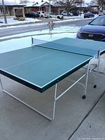 Ping pong table set up outside with green tabletop, white frame and net attached.