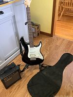 Black Yamaha Pacifica style electric guitar on stand with amp and gig bag on floor
