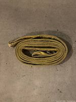 Rolled up yellow nylon lifting sling with reinforced edges on the floor.