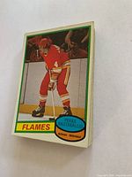 Stack of hockey cards with Pekka Hautakallio card on top showing a Flames player in red uniform, standing on the ice with hockey stick.