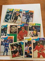 Photo showing 11 1983-84 O-Pee-Chee hockey cards arranged on white paper featuring NHL players such as Stastny, Foster, Boutette, Boldirev