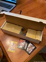 Open box containing a large number of baseball cards stacked closely together with some sample cards spaced in front.