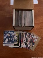 Photo of cardboard box filled with over 100 hockey cards in sleeves and cards fanned out on table to show variety.