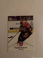 Front image of Connor McDavid 2015 ITG Young Stars hockey card showing player in black and red jersey skating with hockey stick.