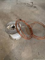 Photo of two metal spools, one wound mostly with white insulated wire and a coil of bare copper ground wire on top, showing cable labeling details.