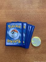 Pile of Pokemon cards facedown with collectible coin next to it on wooden surface