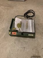 Full view of the Proxxon mini table saw with power cord, plastic miter gauge, and clear guide fence on top