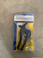 Front view of BrassCraft ratcheting PVC cutter in clear blister packaging with cardboard backing. Shows tool and product label in English, Spanish, and French.