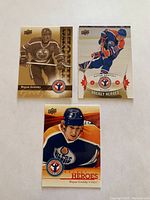 Three Wayne Gretzky hockey cards laid out on a white background. Top left is a gold foil card, top right is a silver-toned card, bottom is a colored Upper Deck card.