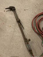 Close-up of metal cutting torch handle showing trigger, adjustment knobs, and attached hoses.