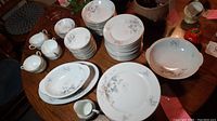Full view of assembled china set on table showing dinner plates, sandwich plates, soup bowls, serving bowl, cups, creamer, and trays.