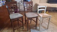 Photo showing all three stools lined up together, two dark wood framed with fabric seats and one white painted wood framed with woven seat.