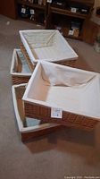 Four large rectangular wicker baskets stacked and lined with white fabric liners, placed on a carpeted floor.