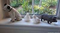 Four animal figurines on window ledge: cast iron dog, two white resin chickens, black cast iron pig
