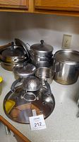 All pots and pans arranged showing lids, handles, and steamer insert on kitchen counter.