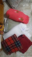 Photo showing five blankets including a pink crocheted blanket with flowers, solid white blanket, red and blue plaid, and solid red blanket with stitching.