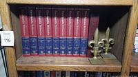 Bookshelf containing a series of Encyclopedia Britannica books with red top and blue bottom binding, along with a pair of brass fleur-de-lis bookends on the right.